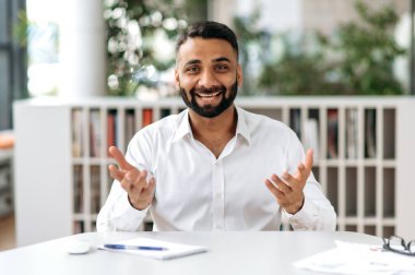 Portre kendinden emin, sosyal, genç, Hintli, serbest çalışan, iş adamı, sakallı üst düzey yönetici, iş arkadaşlarıyla internet üzerinden iletişim kuruyor, elleriyle hareket ediyor.