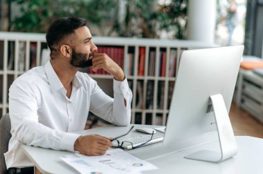 Zeki, kendine güvenen başarılı Hintli işadamı, üst düzey yönetici ya da sakallı CEO bir ofiste oturur, beyaz gömlek giyer, düşünceli bir şekilde bir kenara bakar, iş stratejisi ya da proje üzerine düşünür.