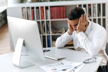 Bitkin düşmüş Hintli şirket sahibi, yönetici ya da ofis çalışanı, masasında kapalı gözlerle oturuyor, başını ovuyor, fazla mesaiden dolayı stresli ve yorgun hissediyor, dinlenmesi gerekiyor.