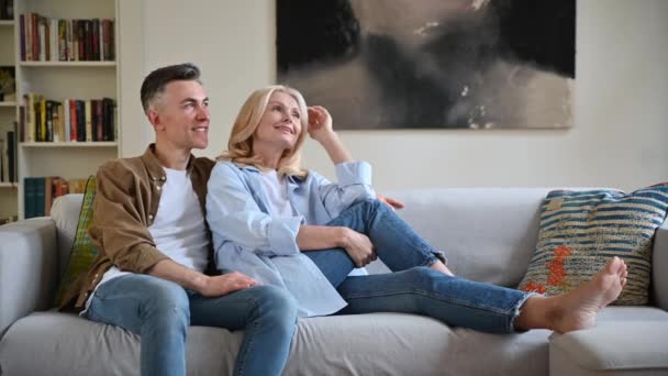 Loving happy adult married caucasian couple in stylish casual clothes, happy husband and wife sitting on the comfortable sofa in the living room, chatting, spending time together at home — 图库视频影像