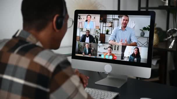 Videoconferência online, reunião distante. Visão lateral de um homem hispânico com um fone de ouvido se comunicando com parceiros de negócios, discutindo um projeto, realiza uma consulta, pessoas multiétnicas em uma tela — Vídeo de Stock