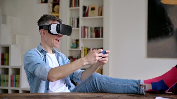 Hombre caucásico de mediana edad, freelancer, con gafas de realidad virtual durante el descanso de trabajo. Hombre excitado probando gafas VR mientras se sienta en el escritorio, teléfono inteligente con auriculares VR, realidad virtual — Vídeo de stock