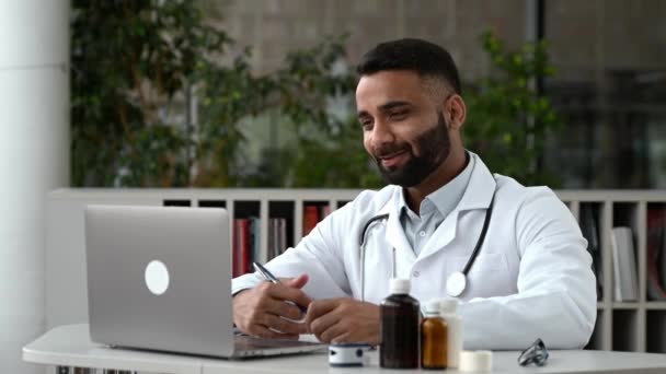 Médico indio lleva a cabo una consulta en línea. Un médico general se comunica con su paciente a través de una videollamada usando una computadora portátil, le receta tratamiento, responde preguntas, hace recomendaciones — Vídeo de stock