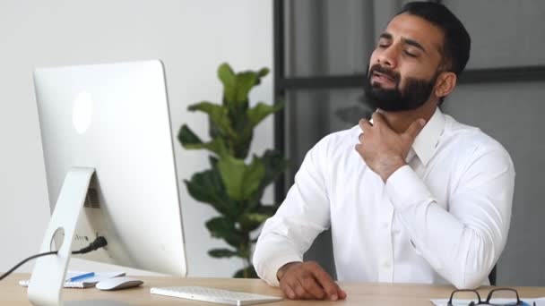Перегруженный работой индийский бизнесмен, менеджер, сидящий за столом в офисе, массирующий шею, уставший от работы, нуждающийся в отдыхе, испытывающий стресс, испытывающий головную боль, мигрень — стоковое видео