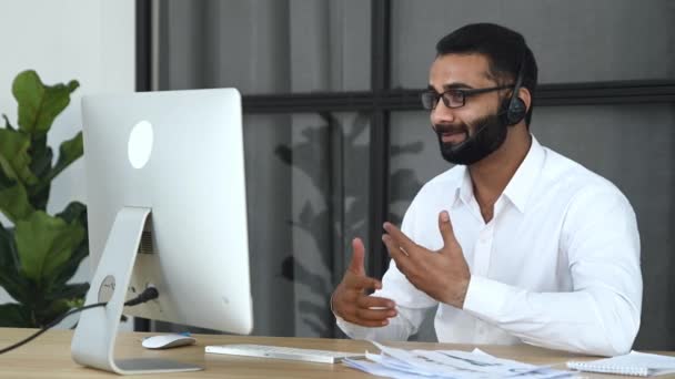Интеллектуальный индийский привлекательный бизнесмен, сидит за столом в офисе, общается через видеоконференцию с деловыми партнерами, показывает финансовый график, обсуждает новый проект — стоковое видео