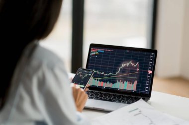 Başarılı akıllı kadın şifreleme tüccarı, dizüstü bilgisayar ve telefon kullanan bir yatırımcı dijital kripto döviz borsası borsasını analiz eder, analiz eder, şifreli paralar alır ve satar.