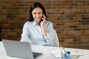 Şirin, dost canlısı, esmer, iş kadını, IT uzmanı, yönetici, bilgisayarın başında oturan, iş arkadaşları ya da müşterileriyle çalışırken akıllı telefondan konuşan, gülen,