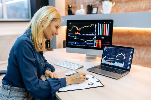 Successful smart mature woman investor and crypto trader, using pc and laptop, analyzes charts of trading in stock market and digital cryptocurrency exchange, conducts analysis, trading crypto coins — Stock Photo, Image