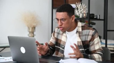 Gözlüklü, serbest çalışan, menajeri olan sinirli İspanyol genç, çevrimiçi konferans sırasında meslektaşlarına duygusal olarak bağırıyor, başarısız oluyor, elleriyle işaret ediyor, çok sinirli ve hayal kırıklığına uğramış.