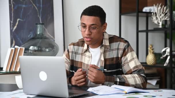 Smart moderner Latino-Typ, Freiberufler, Manager oder Student, sitzt an seinem Schreibtisch, benutzt einen Laptop für die Online-Kommunikation, spricht über Videokommunikation, arbeitet oder studiert aus der Ferne, lächelt — Stockvideo