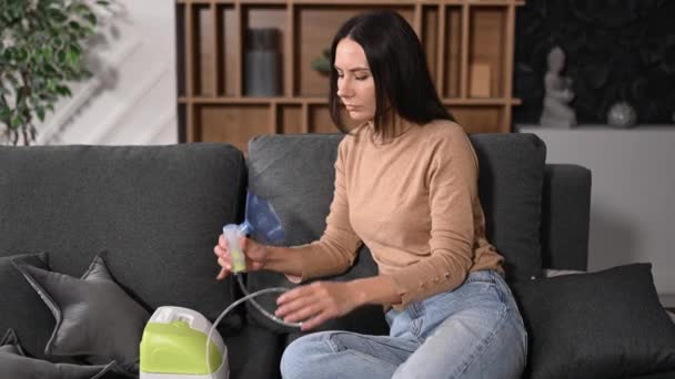 Femme caucasienne malsaine avec un inhalateur, faisant l'inhalation à la maison, elle utilise un nébuliseur et un inhalateur pour le traitement, assise sur le canapé à la maison en quarantaine, maladie, bronchite — Video