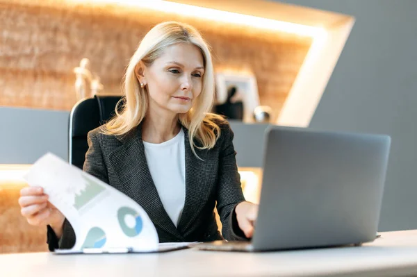 Blanke volwassen invloedrijke succesvolle slimme zakenvrouw, financieel analist, manager, zittend achter een laptop, het bestuderen van documenten, het analyseren van diagrammen en het plannen van financiële strategie — Stockfoto