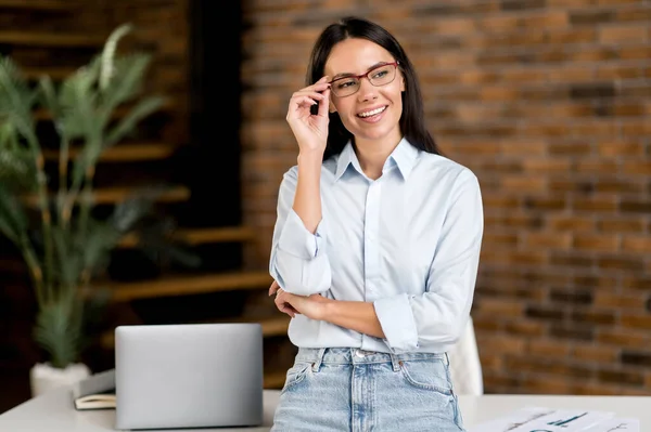 Portret gelukkige succesvolle mooie jonge volwassen blanke zakenvrouw of makelaar staan in de buurt van het bureau in het kantoor, gekleed in stijlvolle kleren, recht glazen, kijken naar opzij, glimlachen — Stockfoto