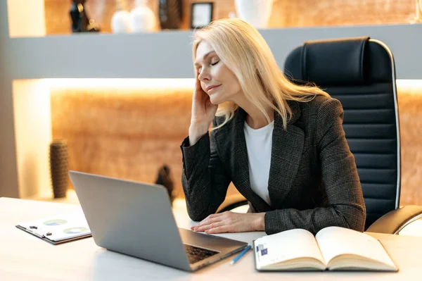 Overworked upset mature businesswoman or top manager, in suit, tired of working online on laptop, experiencing stress and headache, taking break from work, massaging her temple, needs rest,eyes closed — Stockfoto