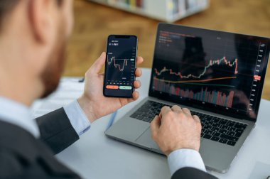 Close-up of a laptop and cellphone screen with stock diagrams. Crypto trader investor broker using cellphone and laptop for cryptocurrency financial market analysis, buying or selling cryptocurrency