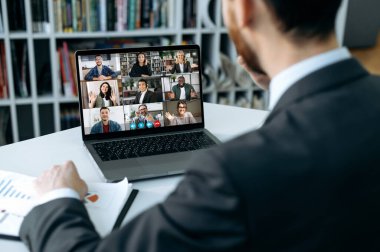 Distant communication. Busy man using a laptop, conducts virtual meeting with business partners on a video call. Group of diverse multiracial business people on laptop screen holding video conference