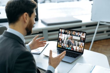 Remote business meeting. Successful man using a laptop, talking to business colleagues on a video call. Group of diverse multiracial business people on laptop screen holding video conference