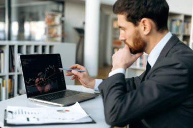 Focused successful trade broker, uses laptop to analyze financial cryptocurrency market, invest in e-currency, buy or sell crypto coins, analyze financial data, develop financial strategy, planning
