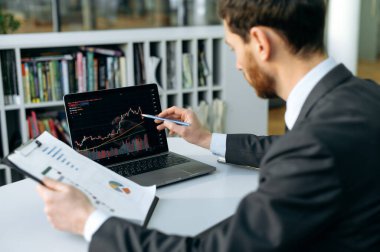 Concentrated smart caucasian broker investor, uses laptop to analyze financial cryptocurrency market, invest in e-currency, buy or sell crypto coins, analyze financial data, develop financial strategy