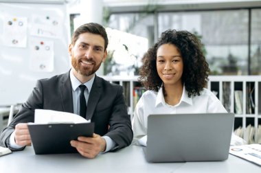 Successful multi-ethnic business people. Confident successful caucasian department head of company, african american female top manager, are looking at camera, smile friendly, sitting in modern office