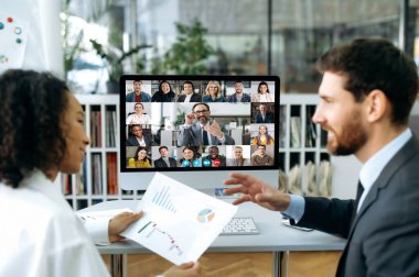A group of business partners gathered in an online video conference to discuss the companys financial plans. Business man and woman of different nationalities talking on video call with colleagues