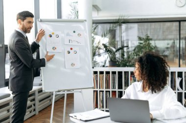 Bir proje üzerinde çalışıyorum, finansal bir strateji geliştiriyorum. Beyaz adam, şirket başkanı, Afrika kökenli Amerikalı kadın meslektaşına stratejisini sunuyor, modern ofiste beyin fırtınası yapıyor.