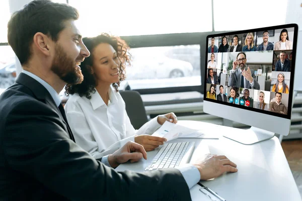 Online video conference of business people. Two business partners sitting in an office, holding an online meeting remotely with business coworkers, talking on a video call with multiracial colleagues — 스톡 사진