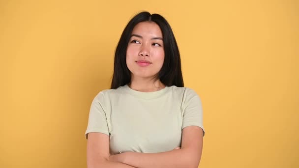 Pensive millennial smart Asian brunette young woman, minded, thinking, creative girl, look up empty space, developing idea, make choice, standing isolated orange background. Shows IDEA sign — Stok video