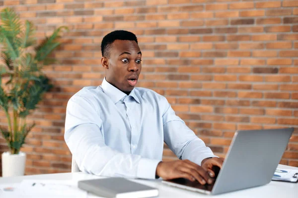 Get unexpected news. African american black shocked man, office employee, CEO, looking in surprise at the laptop screen on modern office, received an unexpected message, amazed facial expression — 스톡 사진