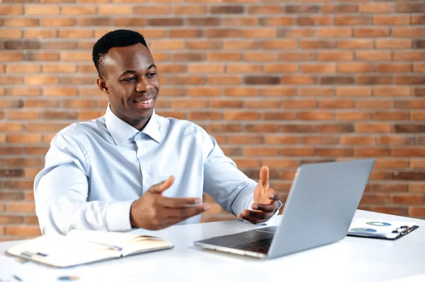 Remote conversation. African american successful business man, ceo company, sales manager, uses laptop for distant communication with client, sits in modern office, gesturing with his hands, smiling — Fotografia de Stock