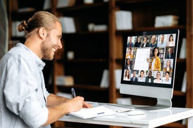 E-learning concept. Positive smart modern Caucasian guy, student or freelancer, listens to an online webinar, lecture, notes information, studies remotely via video conference