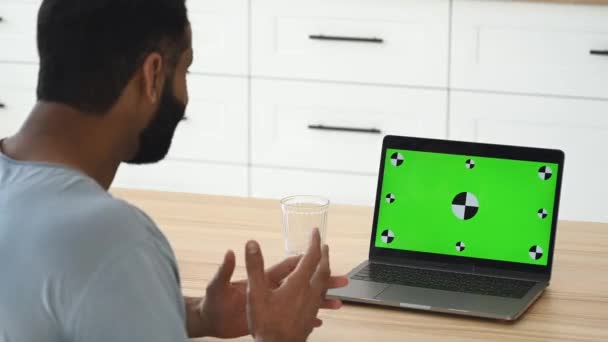 Green screen laptop for your insertion. Over shoulder view of Indian man, freelancer, working remotely from home, using laptop to discuss goals and strategy with colleagues via video conference — Vídeo de Stock