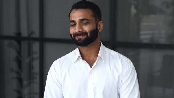 Close-up video portrait of a successful intelligent bearded Indian businessman, manager or IT specialist, ceo company, in modern office, wearing a white shirt, looking at camera with a friendly smile — Video
