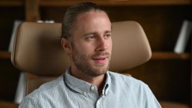 Handsome successful confident caucasian man, entrepreneur, company ceo, IT specialist, top manager, sitting in a chair in his modern office, looking at the camera, smiling friendly