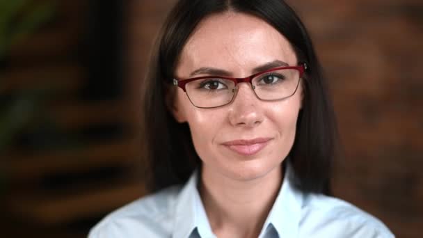 Close-up de adorável feliz mulher de negócios morena caucasiana agradável, executivo da empresa ou gerente corporativo vestindo óculos, em roupas formais, olhando para a câmera, sorrindo amigável — Vídeo de Stock