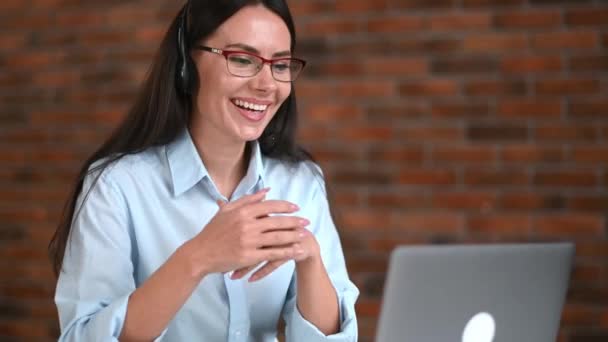 Satisfied happy caucasian businesswoman with glasses and headset, support employee, online consultant, call center operator, using laptop, talking with client or employee, conducts consultation, smile — Vídeos de Stock