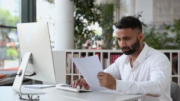 Upset young adult Indian business man, sales manager or financial specialist, work in office using computer, studying documents and graphs, conducting analytics, distressed by bad report,throws papers — Video Stock