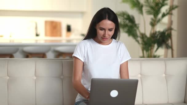 Happy young cute confident brunette caucasian woman, in casual clothes, sitting on sofa, using laptop, celebrating good profit, rejoice news or message, gesturing with fists, looking at screen, smile — Stock Video