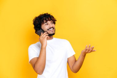 Cep telefonuyla konuşmak. Neşeli, heyecanlı Hintli karizmatik adam hoş bir telefon konuşması yapıyor, mutlu yüz ifadesi, izole edilmiş turuncu arka planda duruyor, el kol hareketi yapıyor, gülümsüyor.