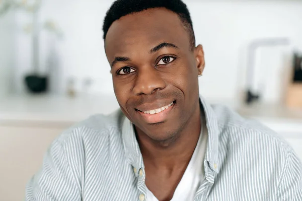 Close-up retrato de um belo jovem bem sucedido de pele escura, afro-americano atraente cara, em roupas casuais, fica dentro de casa e olhando para a câmera, sorrindo amigável — Fotografia de Stock