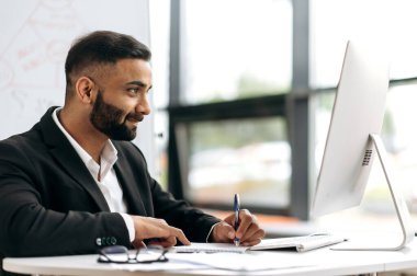 Çekici başarılı zeki Hintli işadamı, şirket lideri, finans danışmanı veya girişimci, masaya oturur, bir iş konferansında beyin fırtınası yapar, ekrana dikkatle bakar, analiz eder,