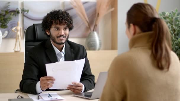 Gerente de Recursos Humanos masculino indio exitoso, empresario, lleva a cabo una entrevista chica en una oficina moderna, usando ropa formal, mirando y escuchando a un candidato de trabajo, sosteniendo un curriculum vitae en las manos — Vídeo de stock