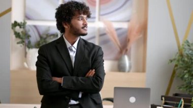 İş elbisesi giymiş başarılı genç Hintli işadamı, yönetici ya da bilişim uzmanı portresi, ofiste kollarını kavuşturmuş, kameraya bakıyor, gülümsüyor.