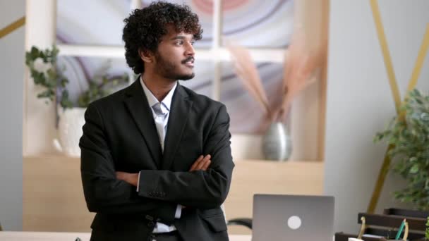 Retrato de negócios de sucesso elegante jovem empresário indiano adulto, gerente ou especialista em TI, vestindo um terno de negócios, fica perto de sua mesa no escritório com os braços cruzados, olha para a câmera, sorri — Vídeo de Stock