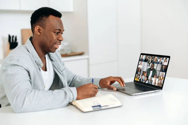 똑똑 한 아프리카 계 미국인 남성 이 노트북을 사용하여 집에 있는 테이블에 앉아 동료나 직원들 과 다종 쌀 비디오 컨퍼런스에 참여하고 있다고 노트를 작성 했다. E-learning 이란 개념입니다. 집에서 하는 일 — 스톡 사진