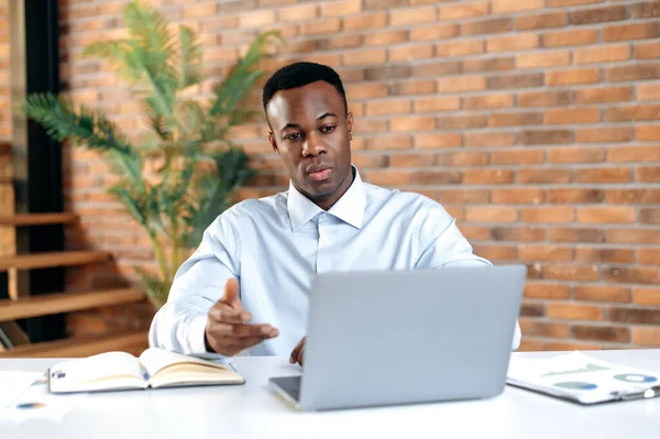 심각하게 혼란 스러워 하는 젊은 아프리카 계 미국인 사업가 , CEO 또는 최고 관리자는 현대 사무실에 앉아 노트북을 사용하고, 온라인 비디오 전화, 비즈니스 전략 또는 보고서, 먼 이야기를 제공 합니다. — 스톡 사진