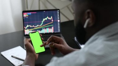 Yeşil ekran modeli. Afro-Amerikan kripto döviz yatırımcısı cep telefonunda yeşil ekran kullanıyor, borsa dinamiklerini analiz ediyor, mobil uygulamaları tarıyor.
