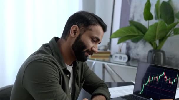 Smart Indian or Arabian man, trader investor, broker, sits in the office, uses laptop for analyze trading charts, predicts the rise or fall of cryptocurrency, thinking. Stock exchange concept — Stock Video