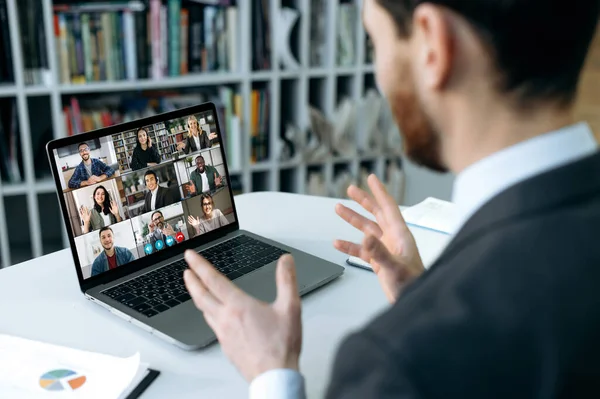 Online training, distant meeting. Caucasian businessman, sits in front of laptop screen in the office, conducts online video meeting with an international business group, explains the working concept