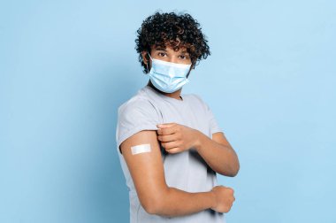 Yüzünde tıbbi koruyucu maske olan ve omzunda yara bandı olan Hintli ya da Arap bir adam aşıyı aldı, kovid 19 ve diğer hastalıklara karşı koruma sağladı.